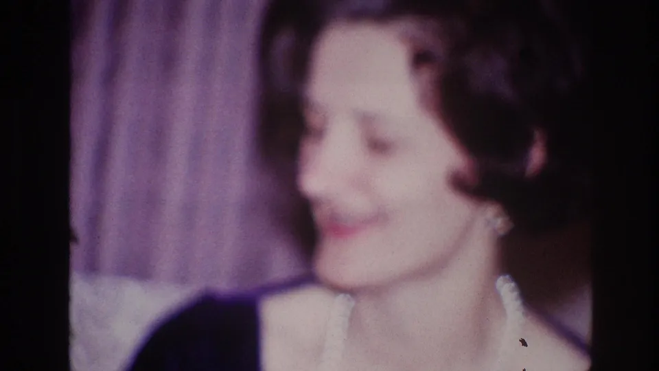 1967 Ottawa frame showing a woman in pearls smiling in profile, with curtains and a private-room background visible.