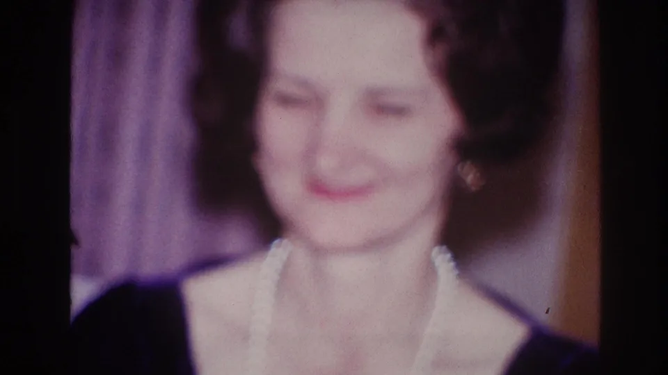 1967 Ottawa frame of a smiling woman in pearls facing toward the camera, with soft focus and interior curtains behind her.