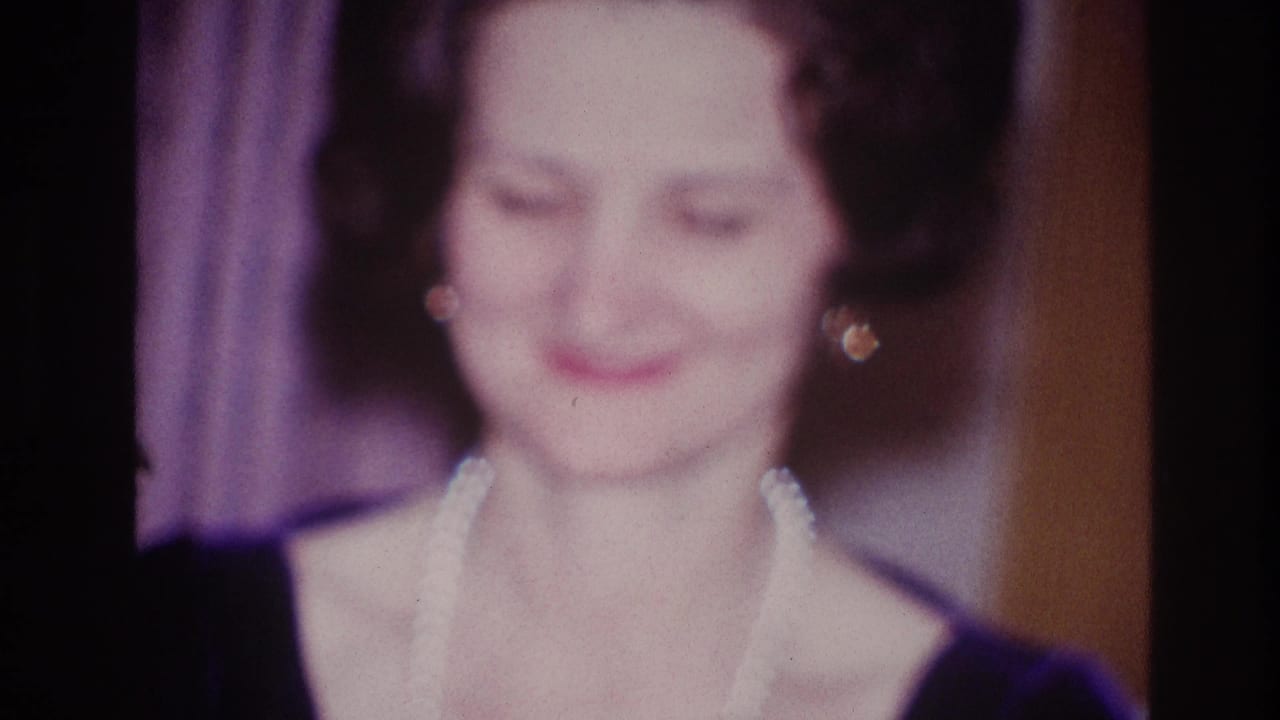 1967 Ottawa home-movie frame showing a woman in a dark dress and pearl necklace smiling in soft 8mm focus.