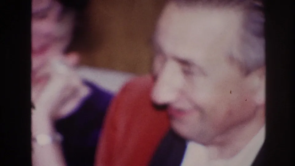 1967 Ottawa frame showing a smiling man in profile with a woman behind him in red and dark clothing.