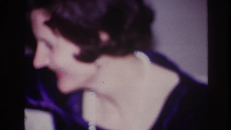 1967 Ottawa frame of a smiling woman in dark clothing, turned in profile during a candid indoor moment.