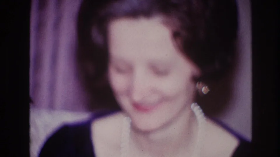 The woman looks down with a slight smile, her pearl necklace and earrings visible against the dark dress in the Ottawa home interior.