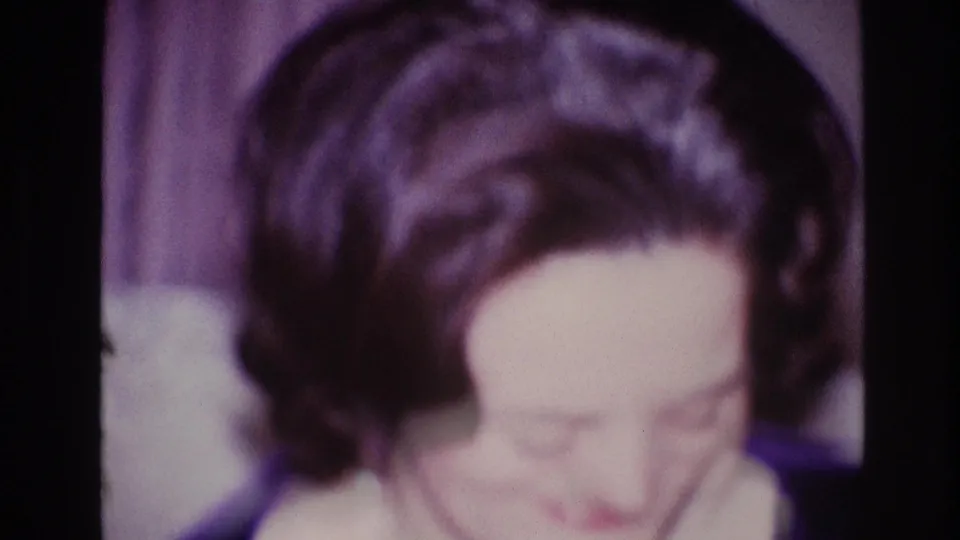 A close, soft-focus frame emphasizes the woman's styled dark hair and lowered expression in the 1967 Ottawa home-movie interior.