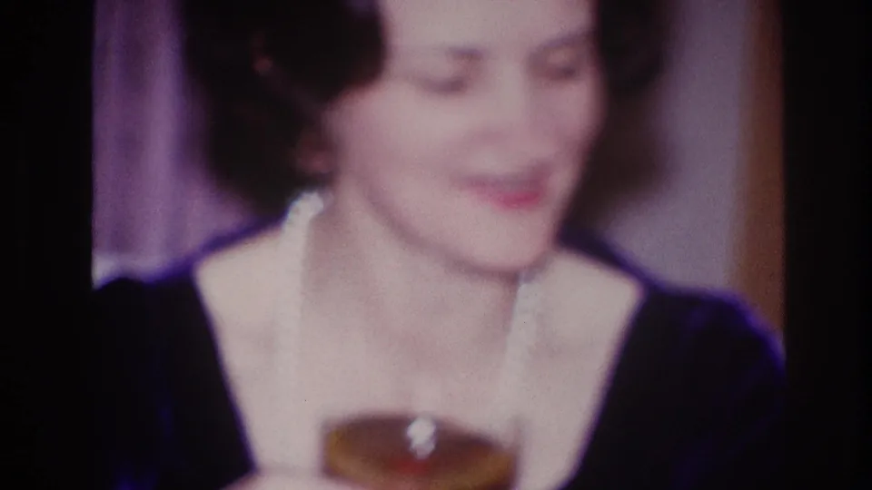 In this 1967 Ottawa home-movie frame, an older woman with styled dark hair smiles in soft focus during an indoor gathering.