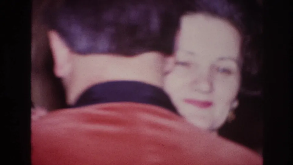 An older man seen from behind dances close with a smiling older woman in this soft 1967 Ottawa home-movie frame.