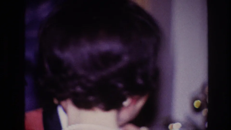 The camera catches the back of the woman's styled hair as the older couple continues dancing in a private 1967 Ottawa interior.