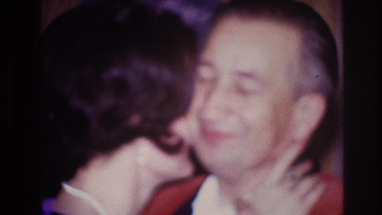 In 1967 Ottawa home-movie footage, a woman leans in to kiss a smiling man wearing a red jacket.