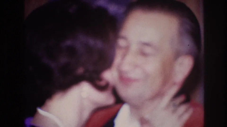 In 1967 Ottawa home-movie footage, a woman leans in to kiss a smiling man wearing a red jacket.