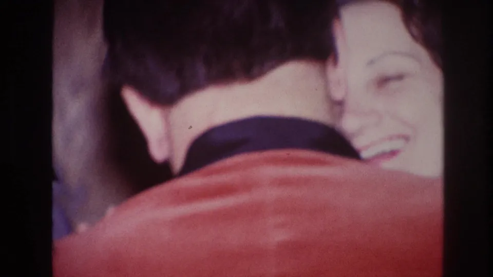 A smiling woman is partly visible over the shoulder of a man in a red jacket in this 1967 Ottawa home movie.