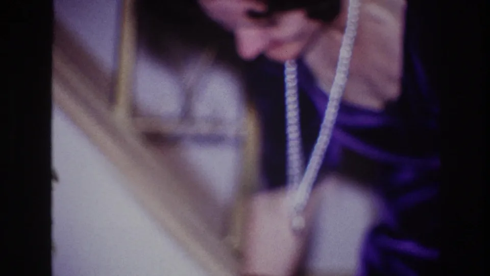 A formally dressed woman wearing a pearl necklace looks down beside a stair rail in 1967 Ottawa home-movie footage.