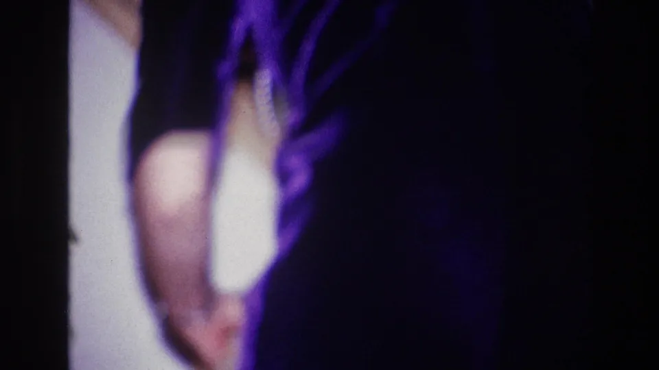 1967 Ottawa home-movie frame showing a partially cropped woman in a dark purple dress standing indoors in soft, low-light focus.
