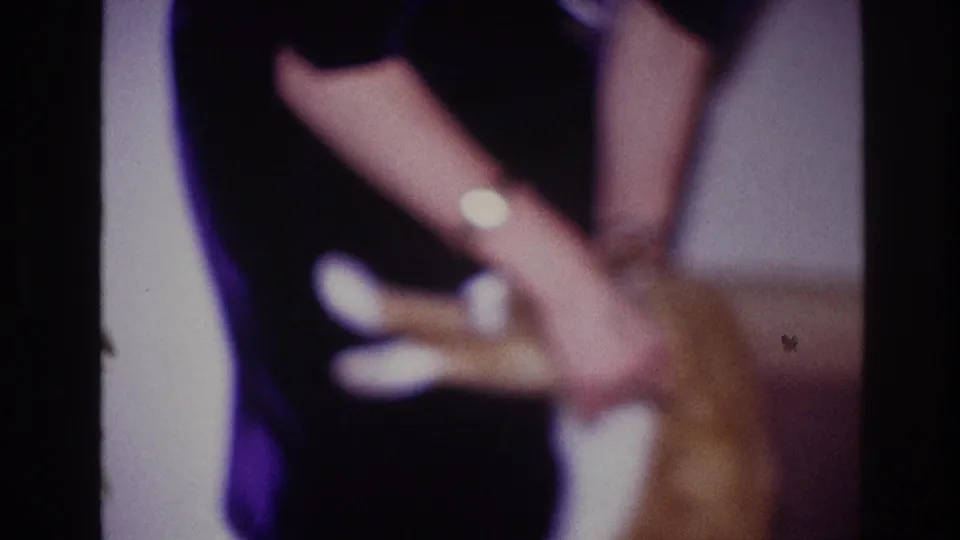 In a 1967 Ottawa home-movie frame, a woman in a dark dress appears to support an orange cat on its hind legs indoors.