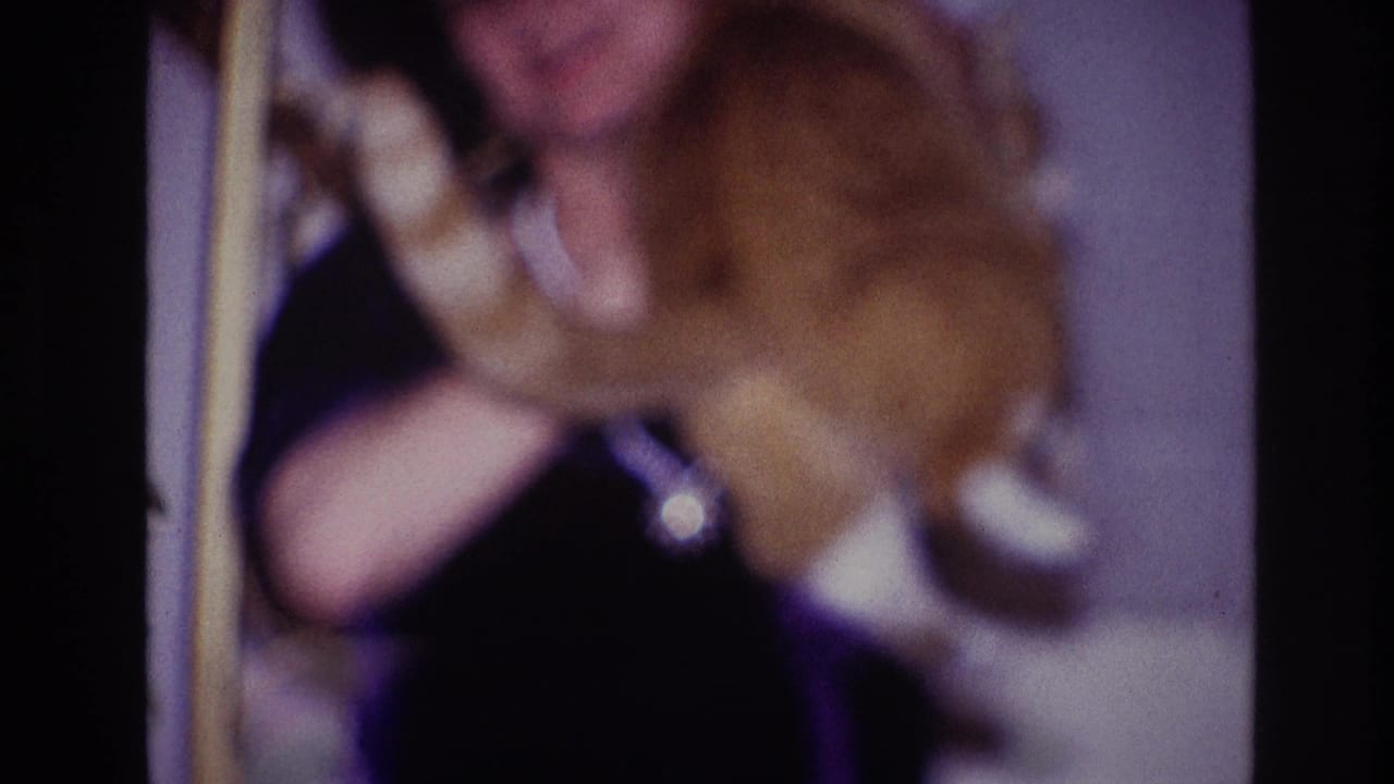 The woman appears seated or leaning indoors while holding the orange cat close, with soft focus and visible 8mm color shift.