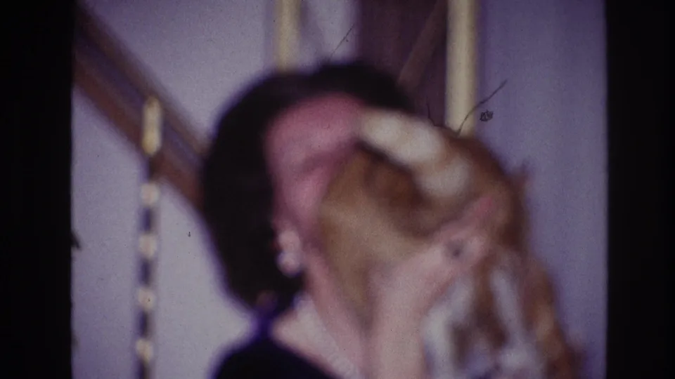 In a soft 8mm Ottawa home-movie frame, the cat turns as the woman holds it close indoors.
