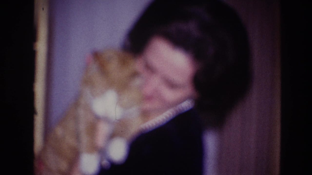 In a 1967 Ottawa home-movie frame, an adult woman wearing a pearl necklace holds an orange and white cat near her face.