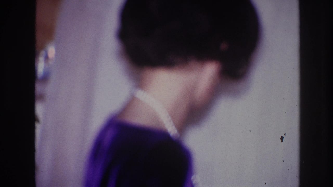 In the 1967 Ottawa home-movie setting, the woman turns away from the camera, with her pearl necklace visible against a dark dress.