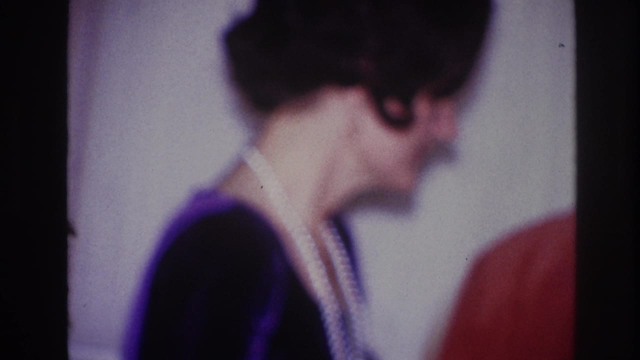The home-movie frame shows the woman in profile, her necklace visible as she turns near another person inside the party room.