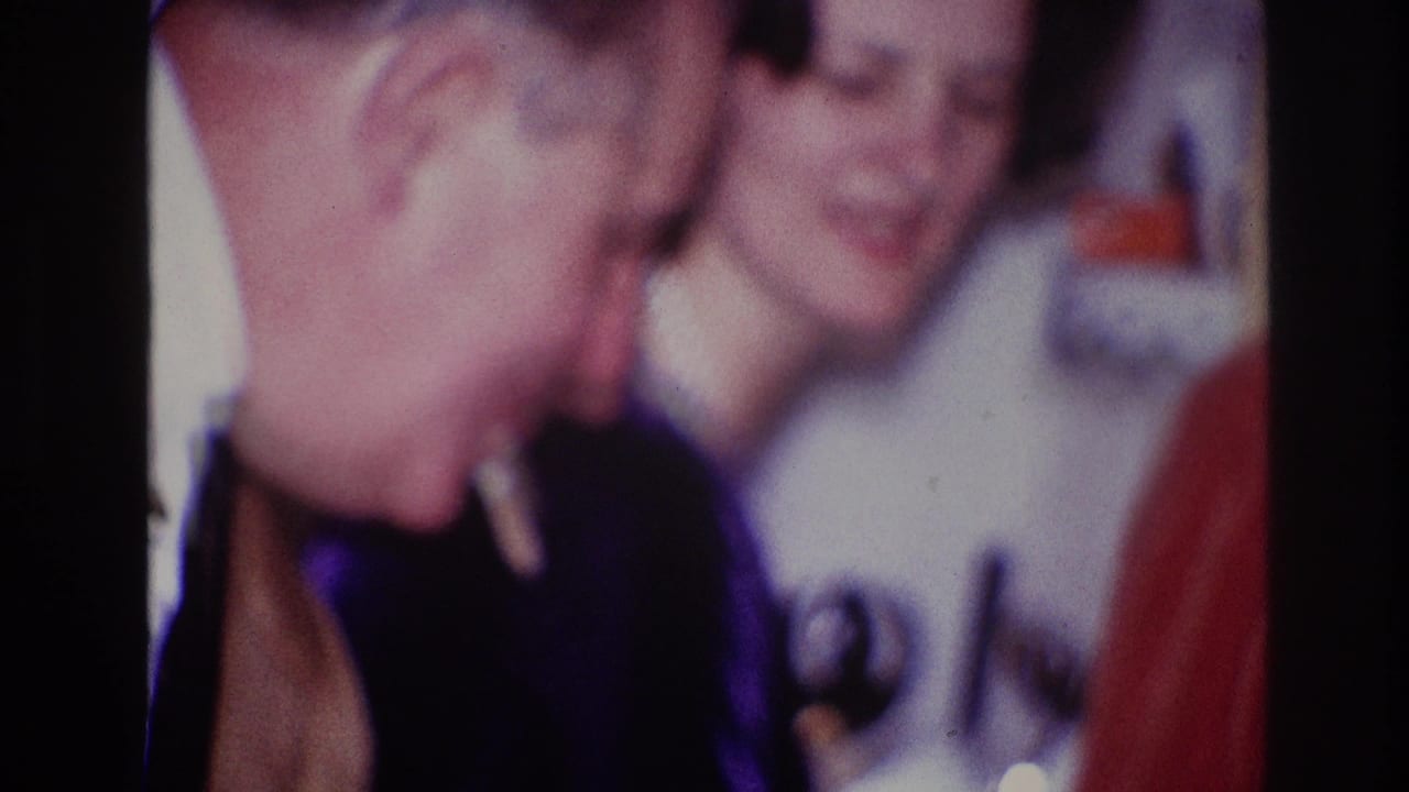 1967 Ottawa 8mm frame showing two adults close together at an indoor dinner party, with a cigarette visible in the foreground.