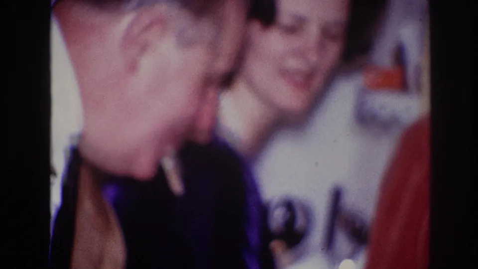 1967 Ottawa 8mm frame showing two adults close together at an indoor dinner party, with a cigarette visible in the foreground.