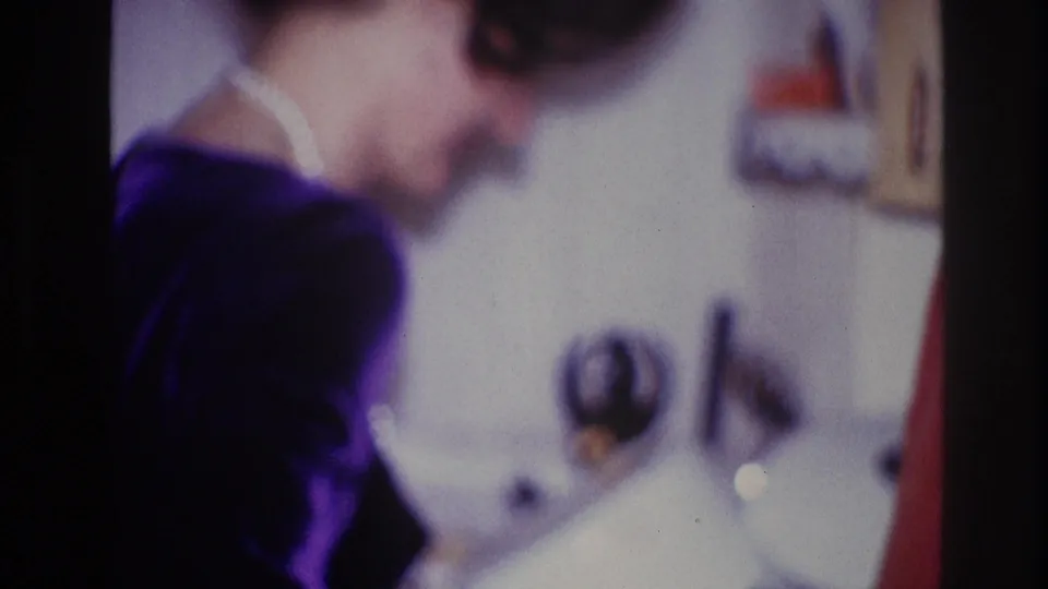 1967 Ottawa 8mm frame showing a woman in a dark top and white collar turning away near an indoor party setting.
