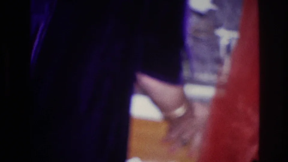 1967 Ottawa home-movie frame of a woman near a table and glass, with another figure partly visible at the edge.