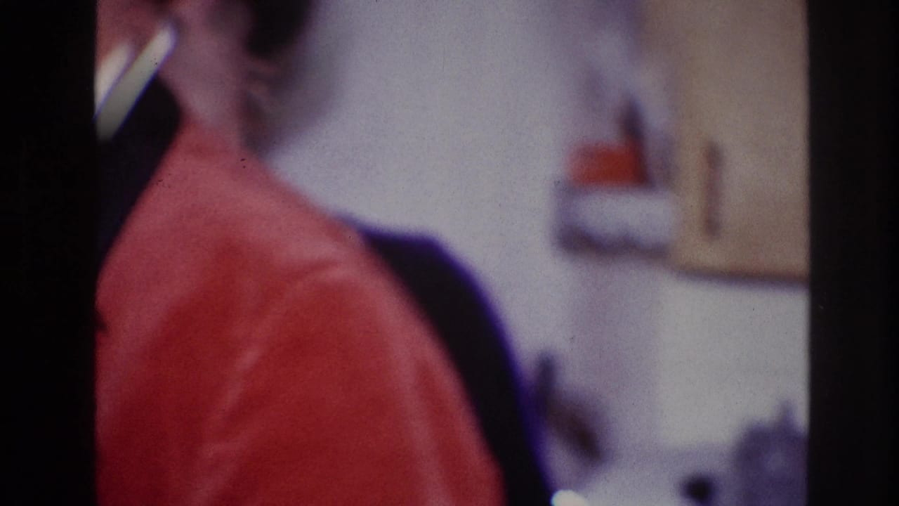 Woman in a red jacket appears in profile inside a private Ottawa interior, filmed in soft 8mm focus.