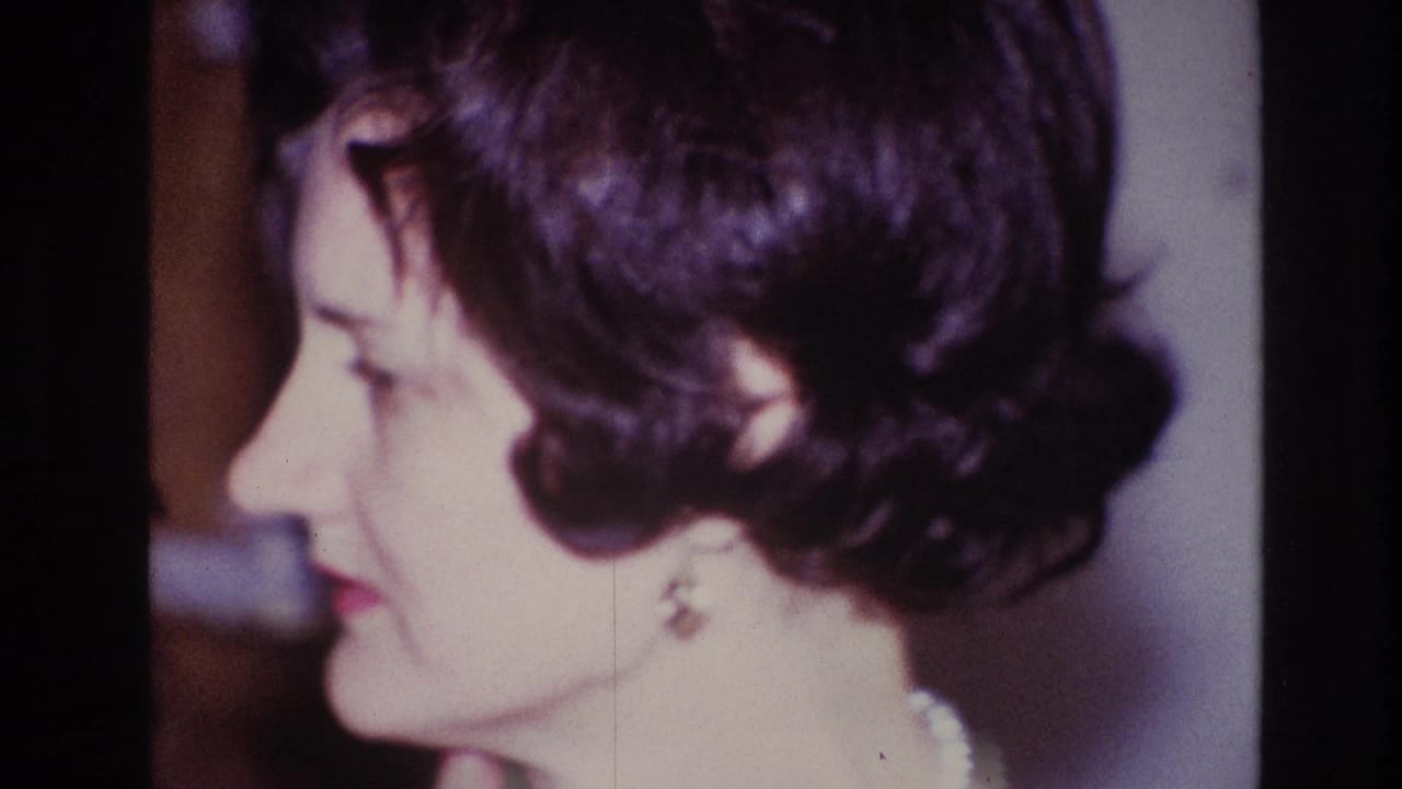 Side-profile 8mm frame of the woman in an Ottawa interior, with short dark hair, earrings, pearl necklace, and soft film grain.