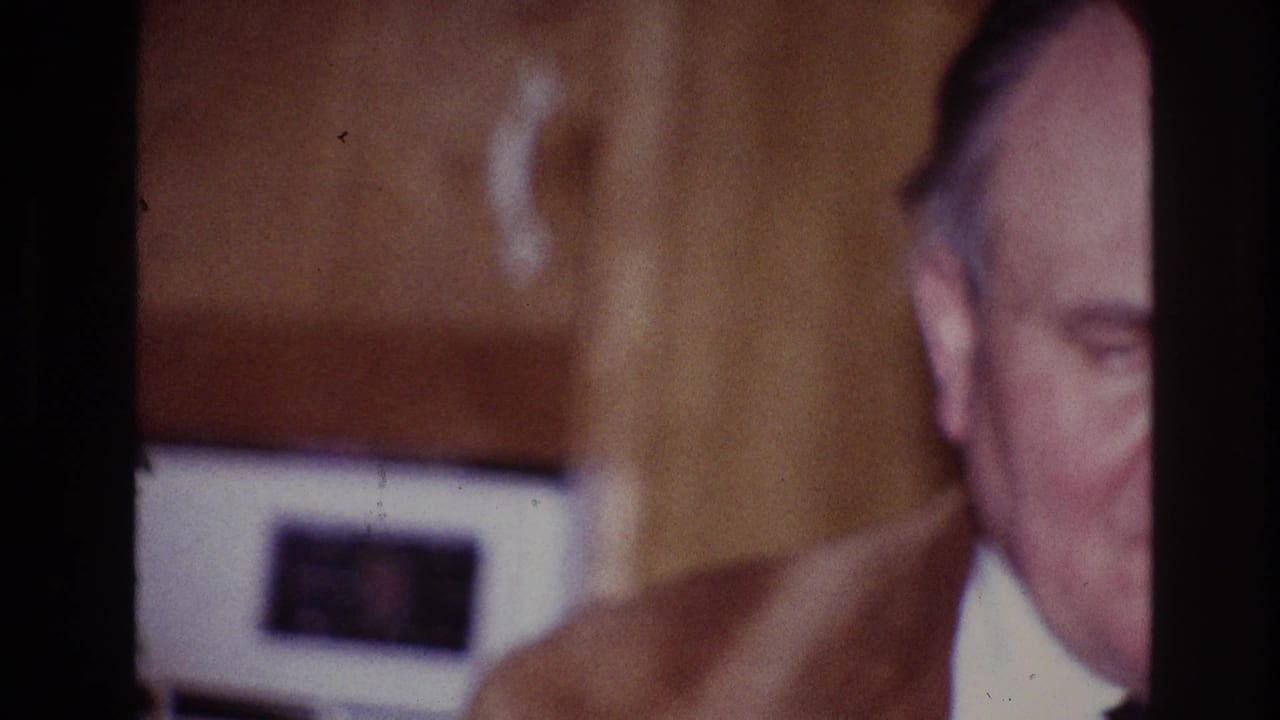 1967 Ottawa home-movie frame with an adult man partly hidden by a dark frame edge and a woman in a purple dress nearby.