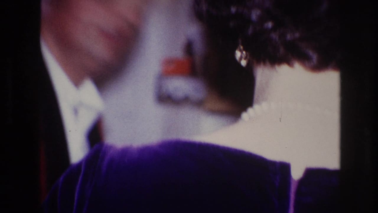 Cropped woman in purple velvet with a blurred man in formal clothing behind her.