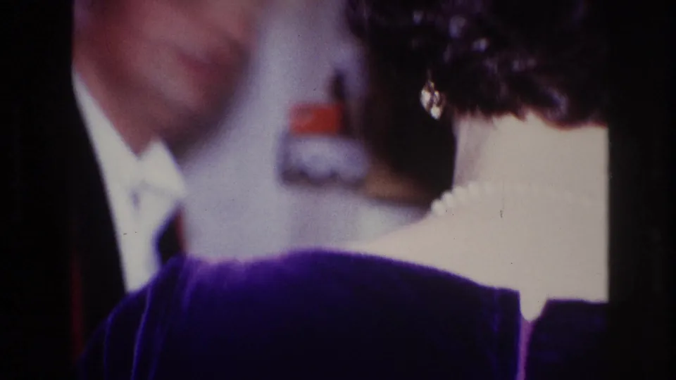 1967 Ottawa indoor frame showing a cropped woman in purple velvet and a softly blurred man in a white shirt behind her.