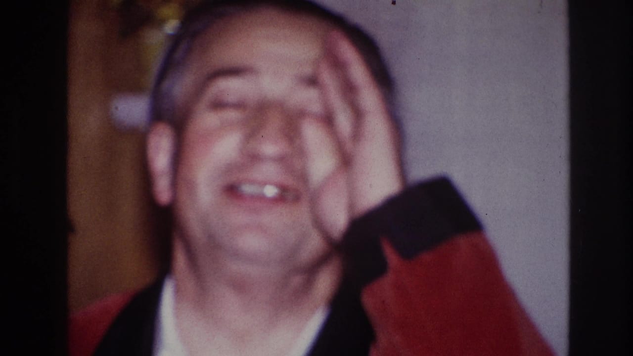 1967 Ottawa indoor frame of the man laughing with one hand over his face, wearing a red smoking jacket and white shirt.