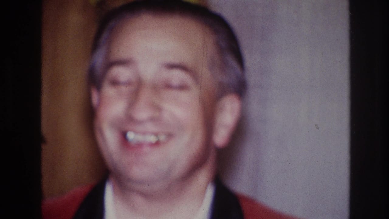 In 1967 Ottawa home-movie footage, an older man in a red jacket smiles in soft focus inside a private interior.