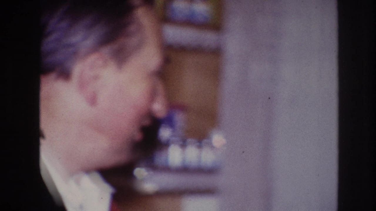 Older man turns in profile beside a blurred interior background.