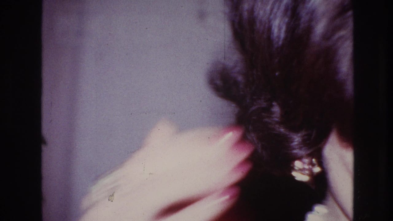 1967 Ottawa home-movie frame showing a close, soft-focus view of dark hair and a hand in an interior setting.