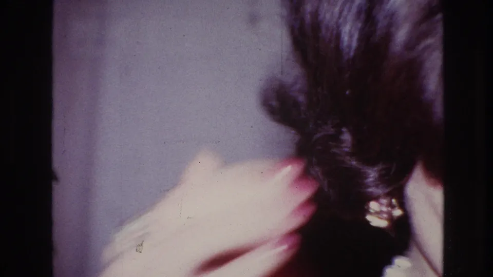 1967 Ottawa home-movie frame showing a close, soft-focus view of dark hair and a hand in an interior setting.
