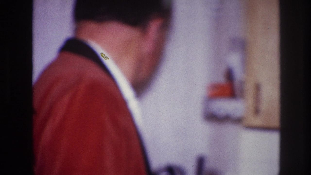 Man in a red jacket and white shirt seen from behind near an interior wall fixture.