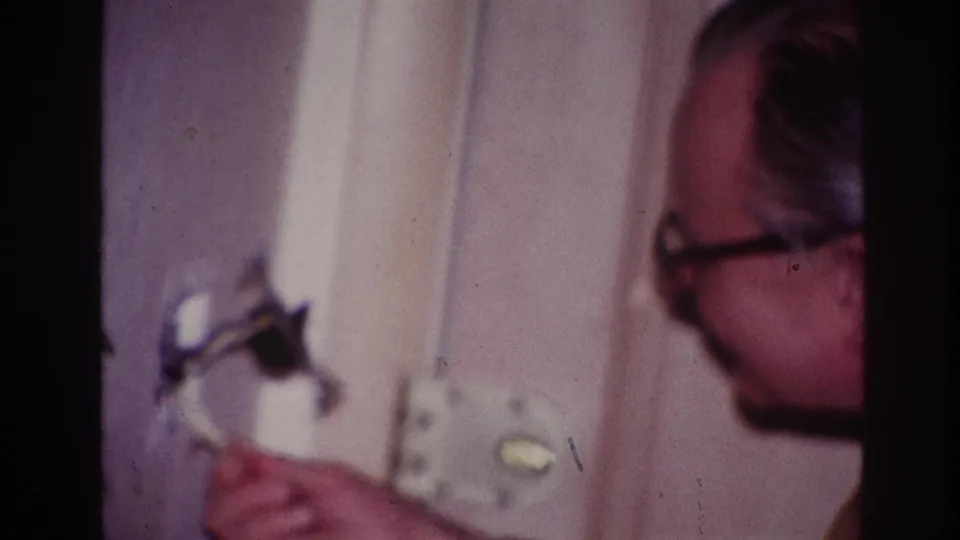 Close side view of the man in glasses facing an interior wall fixture, with soft 8mm color and blur.