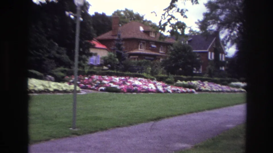 Residential Ottawa view with a brick house, green lawn, sidewalk, lamppost, and pink and white garden flowers.
