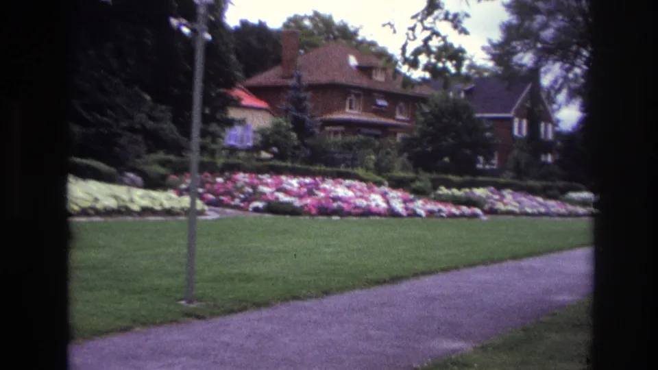 1967 Ottawa residential scene showing a brick house beyond a broad lawn, sidewalk, lamppost, and colorful flower planting.