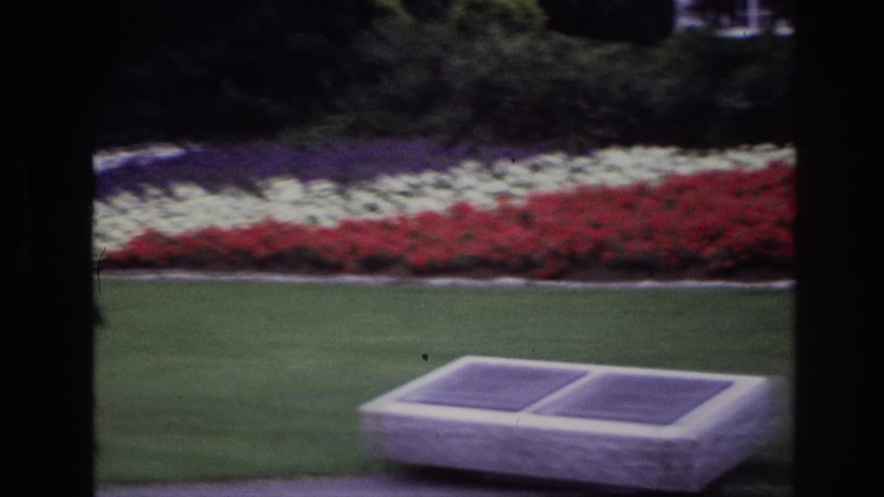 Low stone plaque with two dark panels in front of red and white flowerbeds on a lawn.