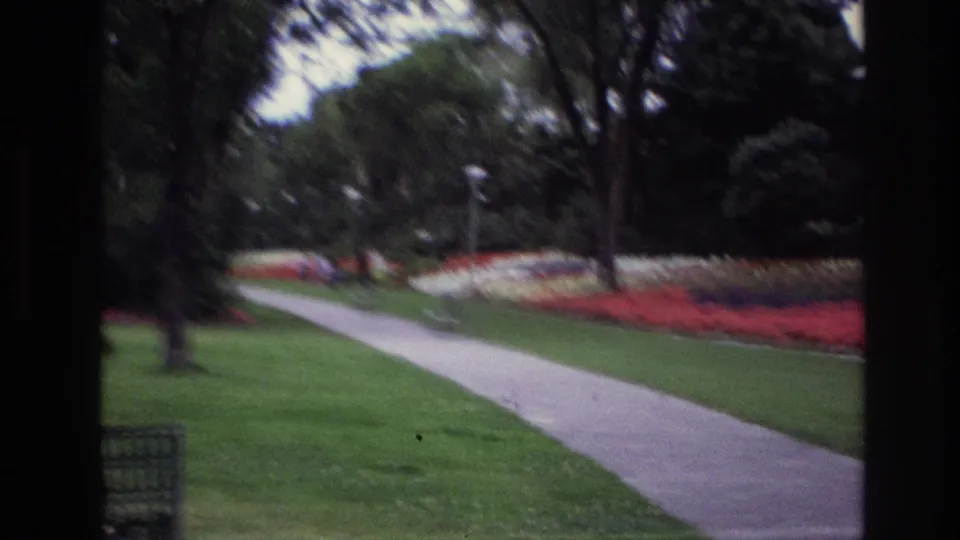 A soft 1967 Ottawa park view shows a pale walkway through grass, red and white flower beds, trees, a bench, and distant visitors.