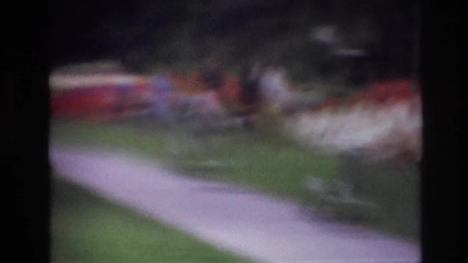 Out-of-focus 1967 Ottawa frame with a curving paved path, lawn, red-and-white plantings, and distant indistinct figures.