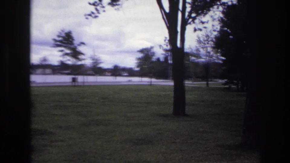 1967 Ottawa park view through a dark foreground frame, showing grass, trees, water, and distant shore under cloudy sky.