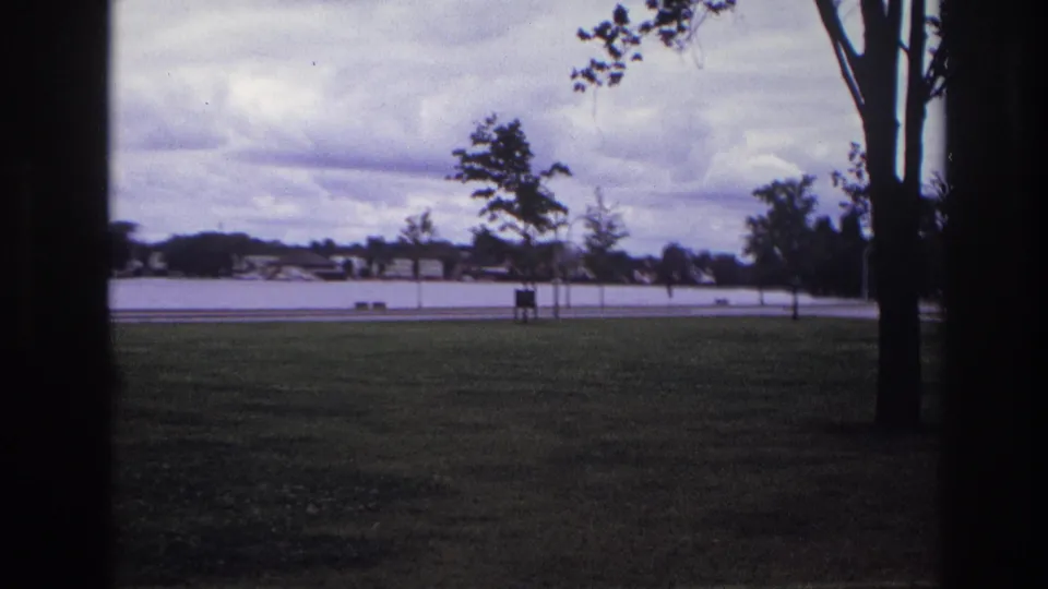 Ottawa waterfront park scene with dark vertical frame edges, grass in foreground, road and water beyond, and distant houses.