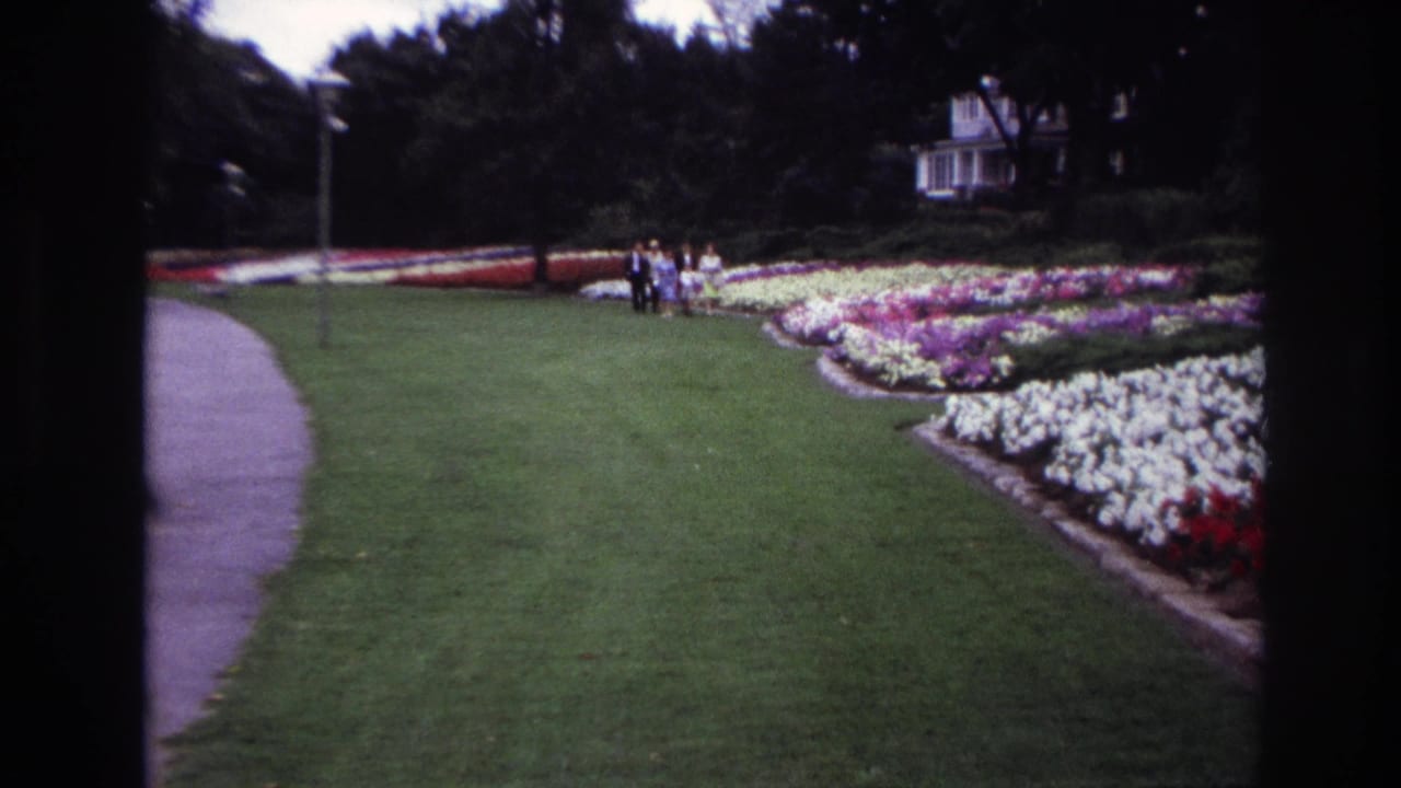 Ottawa 1967 8mm frame with a small group standing or walking near formal garden beds, with a path and white building in the background.