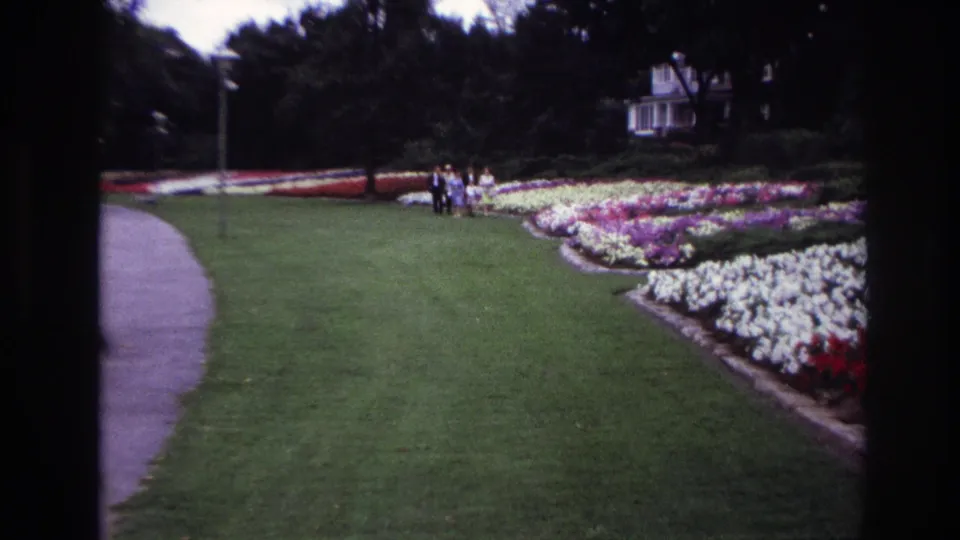 Ottawa 1967 8mm frame with a small group standing or walking near formal garden beds, with a path and white building in the background.