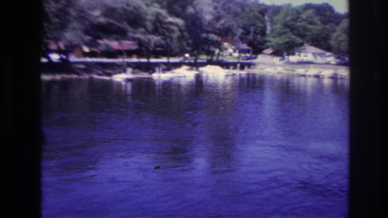1967 Ottawa home-movie view across blue-tinted lake water toward a forested recreational shoreline.