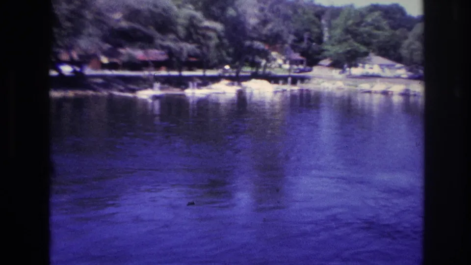 1967 Ottawa home-movie view across blue-tinted lake water toward a forested recreational shoreline.
