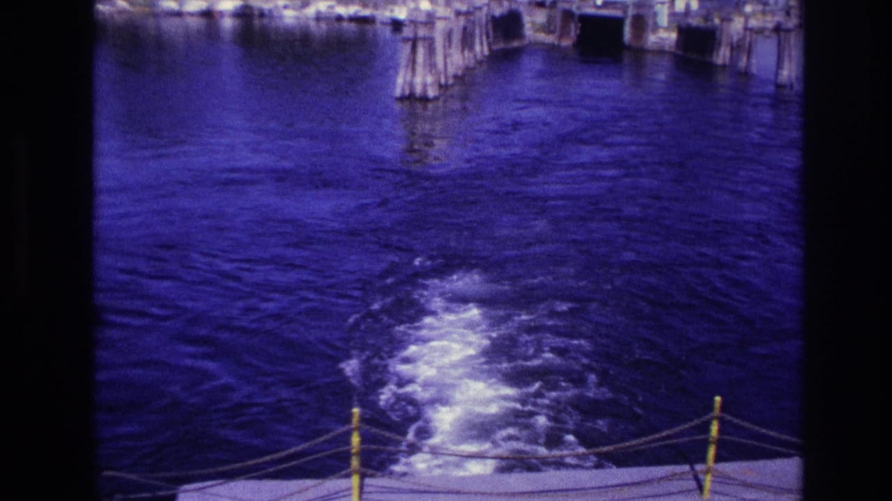 Boat stern view of foaming wake moving away from wooden piers.