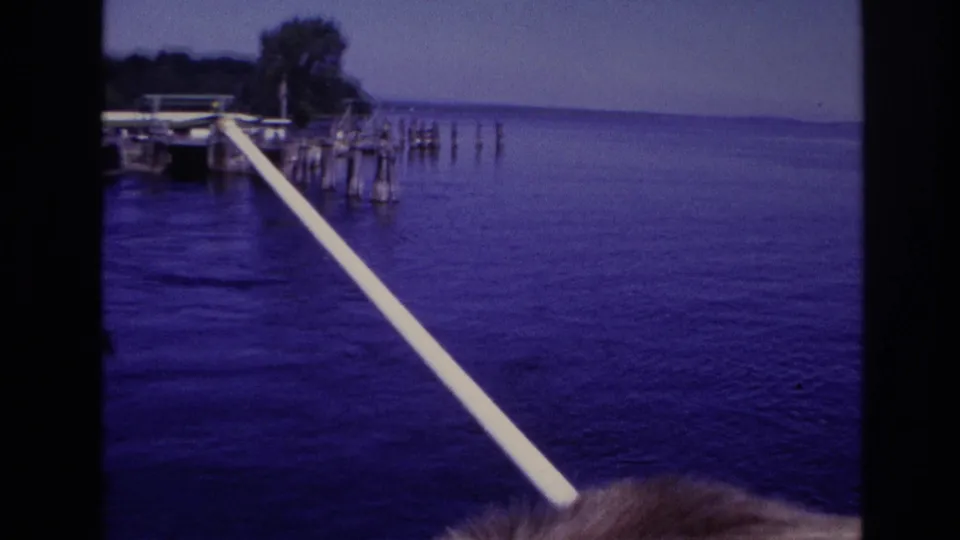 1967 Ottawa-area 8mm frame from a boat, showing dock structures at left, calm water, a white rail, and a partial passenger at the lower edge.